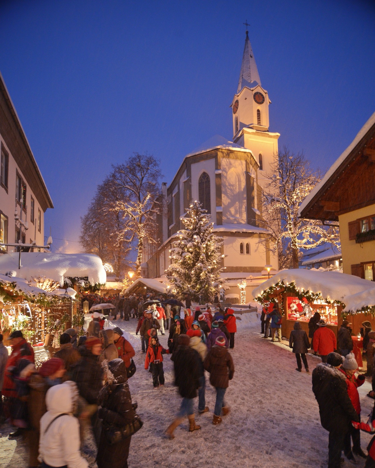 Bad Hindelang zur blauen Stunde: beleuchtete Dorfkirche über dem winterlichen Weihnachtsmarkt