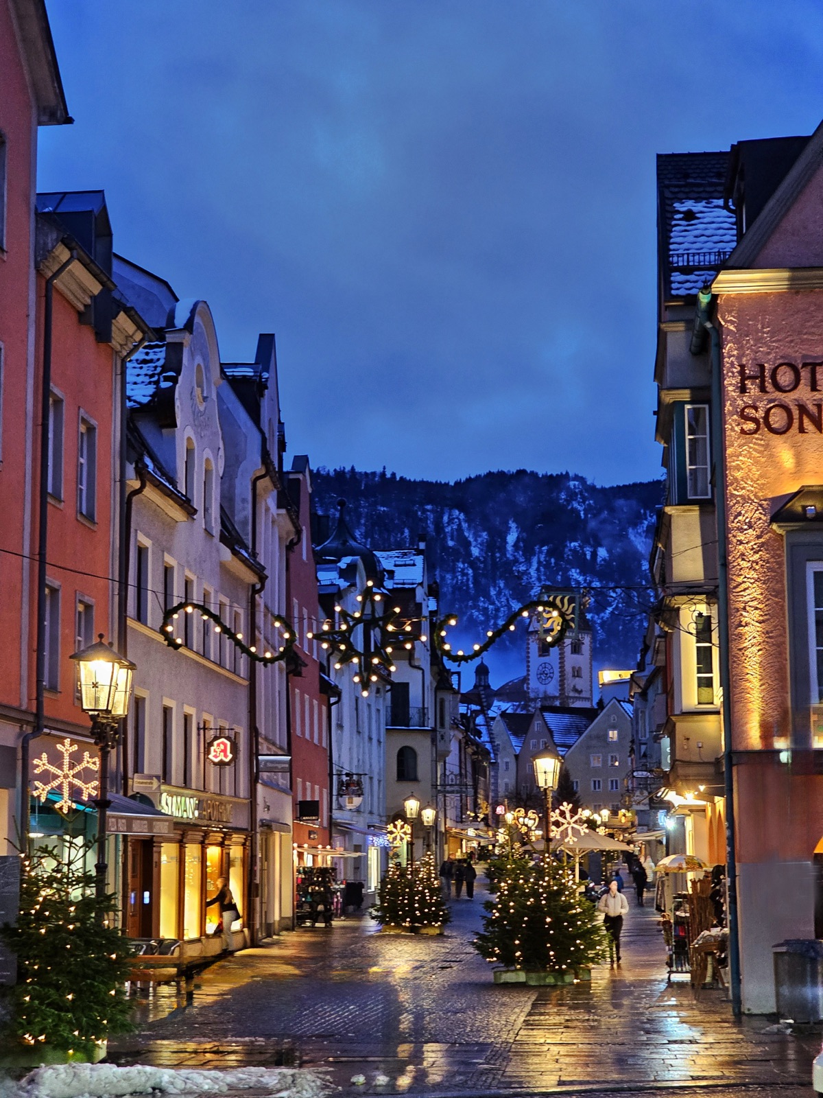 Füssens Altstadt zur blauen Stunde: winterlich beleuchtete Gasse mit Blick auf das Bergpanorama