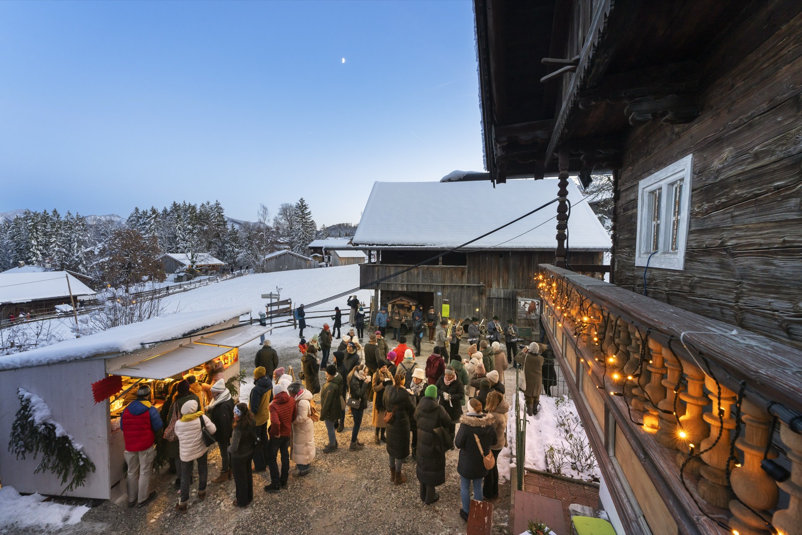 Blaskapelle vor schneebedecktem Bauernhaus beim Winterabend im Freilichtmuseum Glentleiten