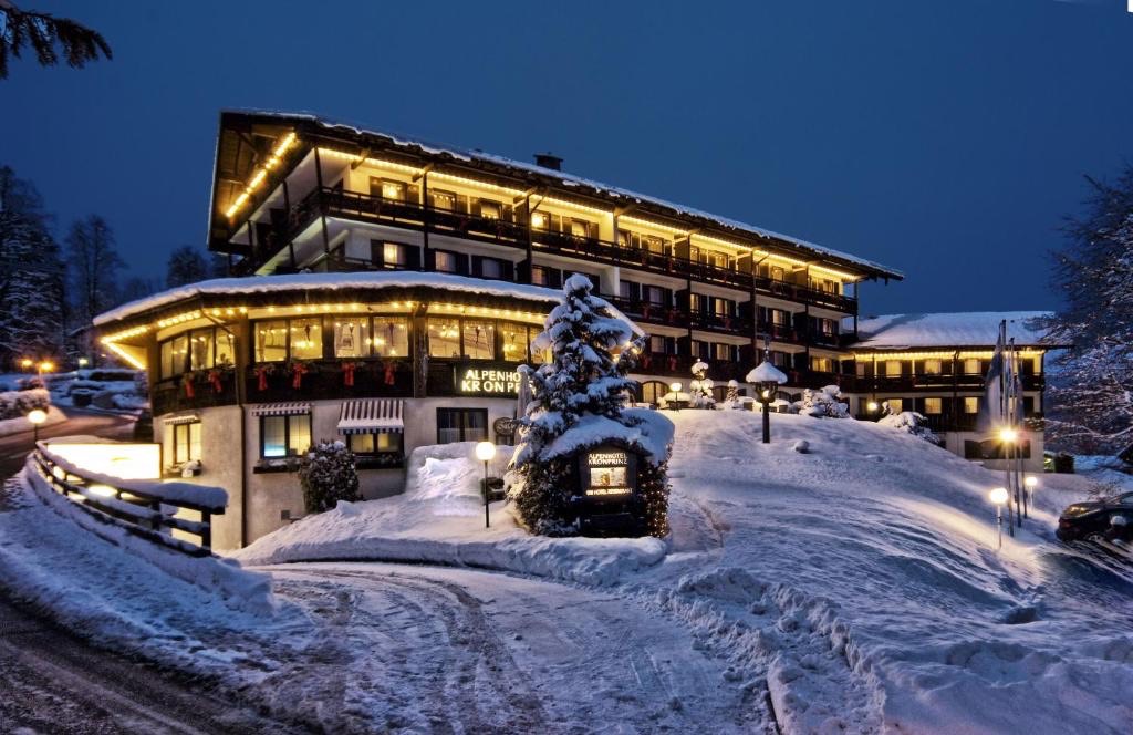 Alpenhotel Kronprinz am Winterabend, beleuchtetes Hotel mit verschneitem Tannenbaum davor