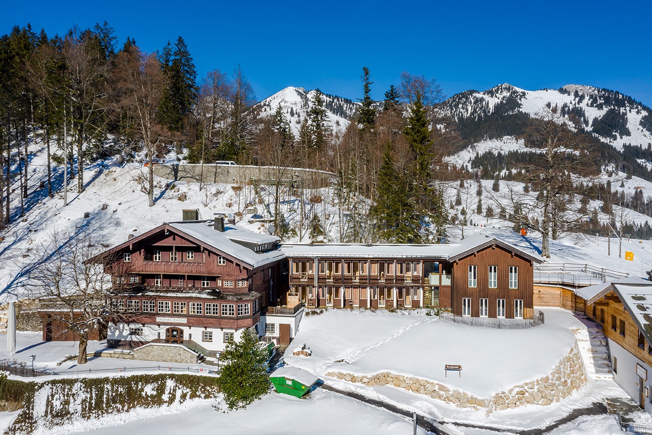 Berghotel Sudelfeld im Schnee, holzverkleidetes Haus vor verschneiten Bergen bei blauem Himmel