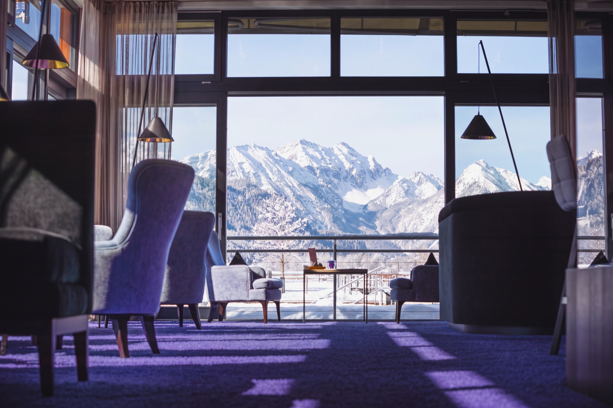 Lounge im Hotel Das König Ludwig mit Sesseln vor bodentiefen Fenstern, dahinter die verschneiten Allgäuer Alpen
