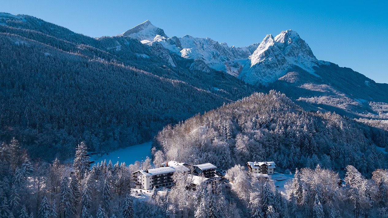 Riessersee Hotel im verschneiten Wald, dahinter der zugefrorene See und das Wettersteingebirge